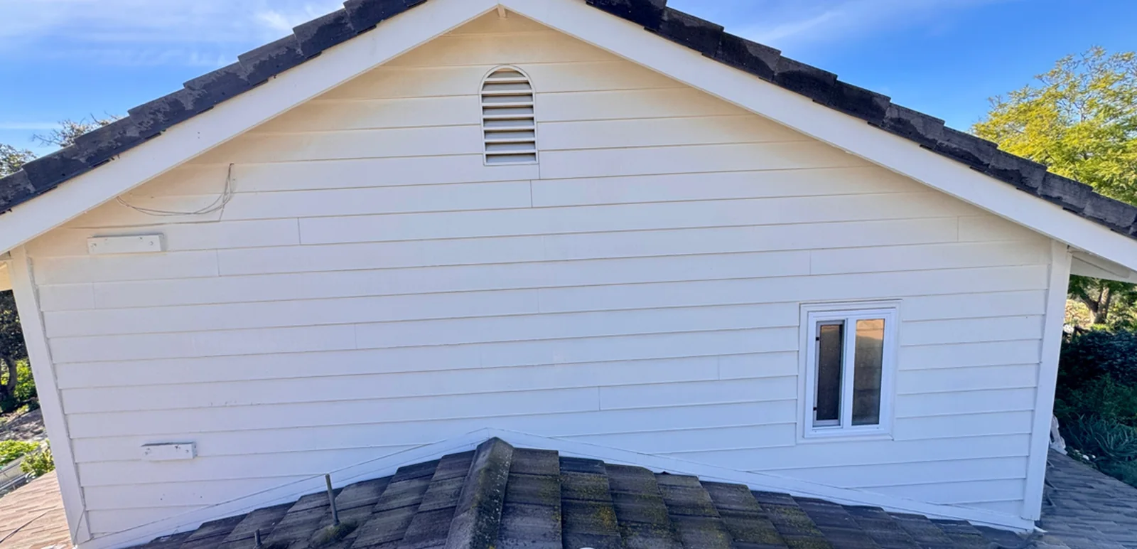 Light-colored house siding in the after frame of an owner-supplied cleaning comparison